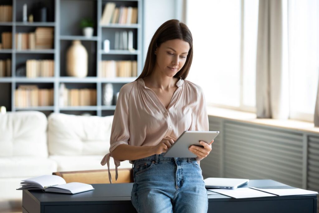 Frau steht im Büro und schaut auf Tablet.