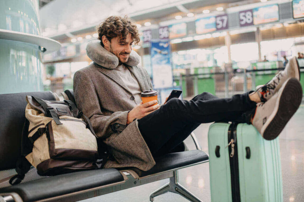 Mann sitzt mit Handy und Kaffee am Flughafen und wartet.