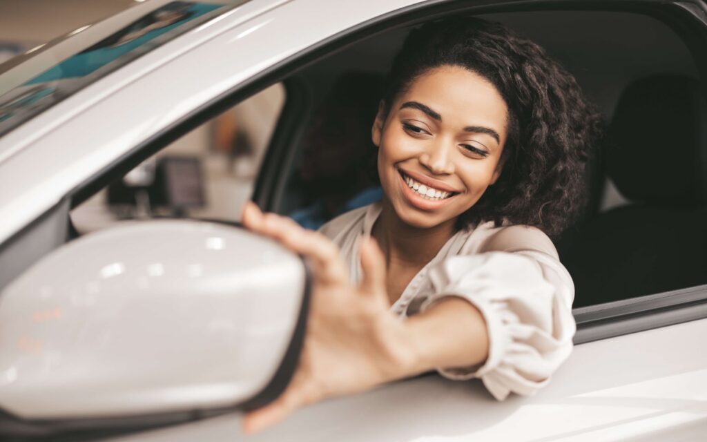 Lächelnde Frau im Auto blickt in den Seitenspiegel