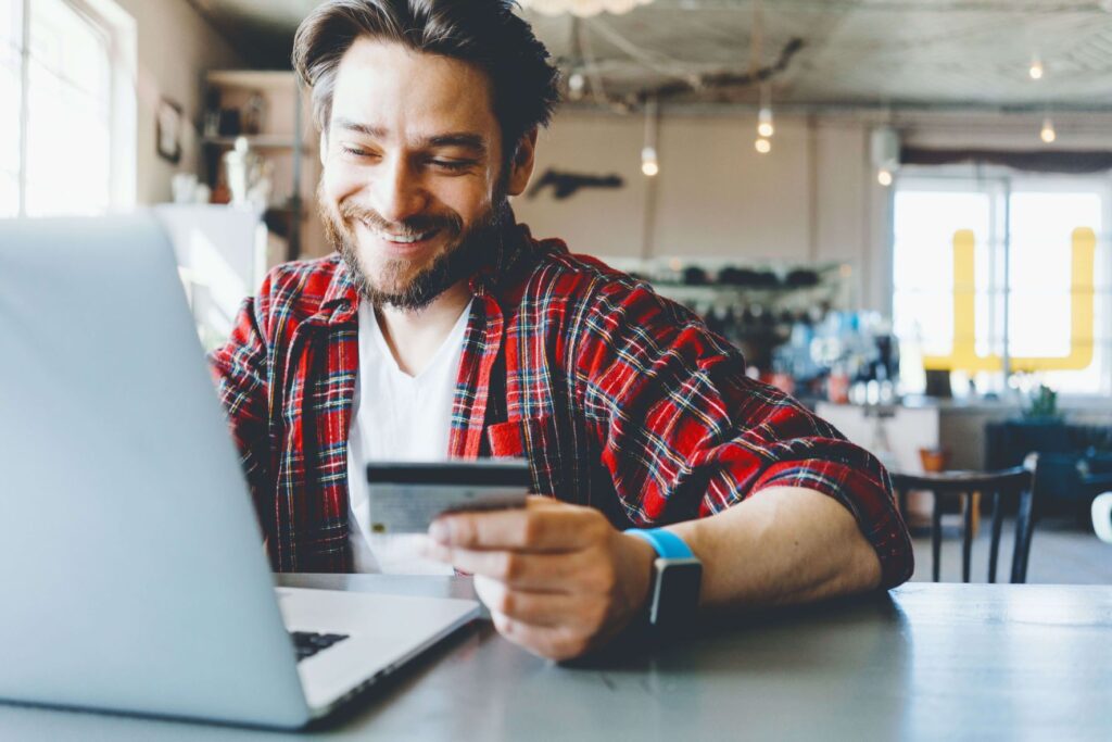 Lächelnder Mann mit Kreditkarte am Laptop