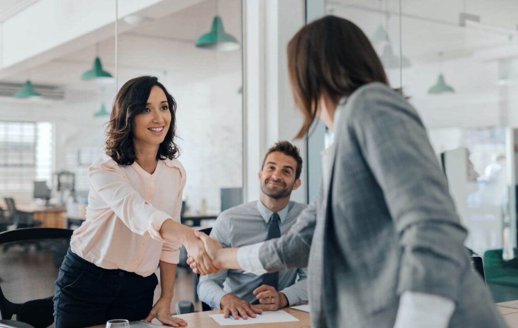 Bewerberin und Arbeitgeberin schütteln sich beim Vorstellungsgespräch die Hände.