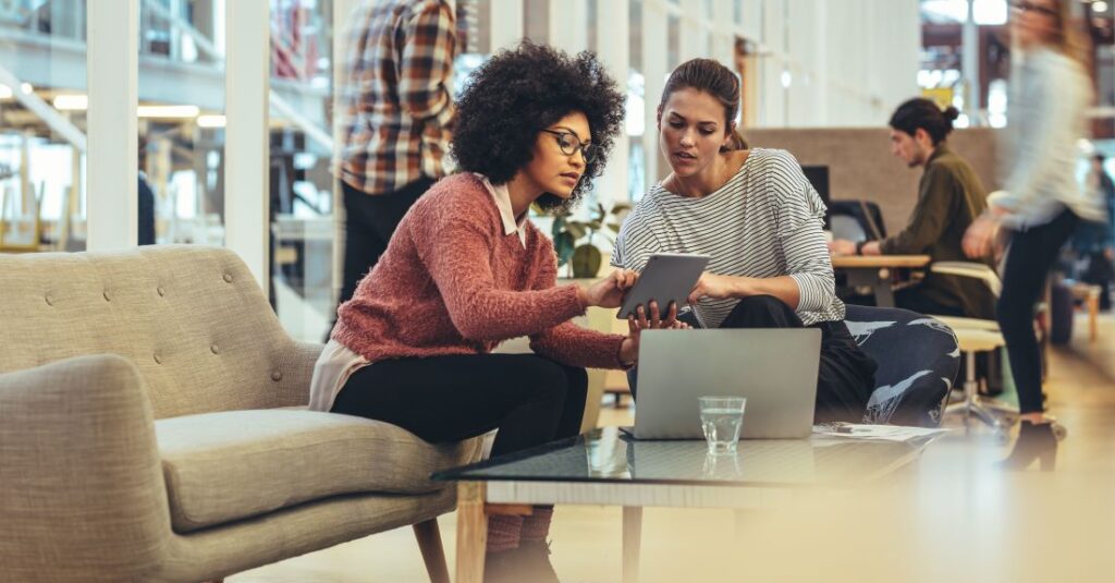 Office Management zwei Frauen in einem Büro betrachten ein Tablet und besprechen die Arbeit.