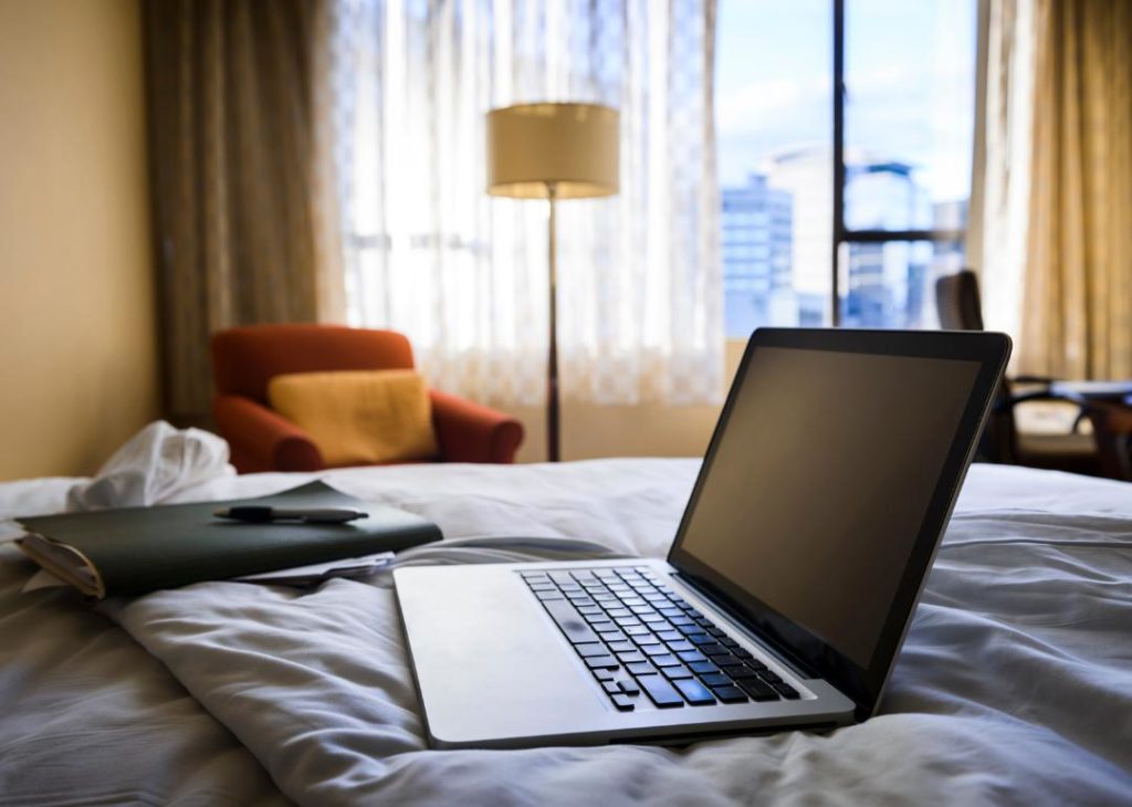 Laptop and business folder on the bed in a hotel room.