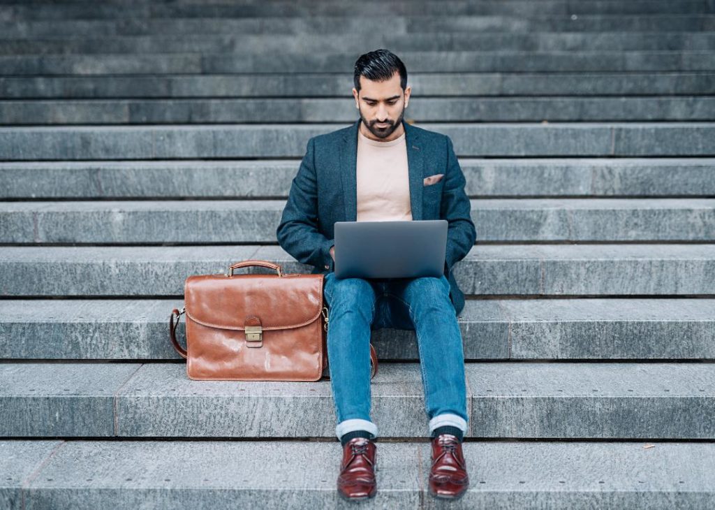 #12. India A man with a leather briefcase sitting on steps while working on his laptop.