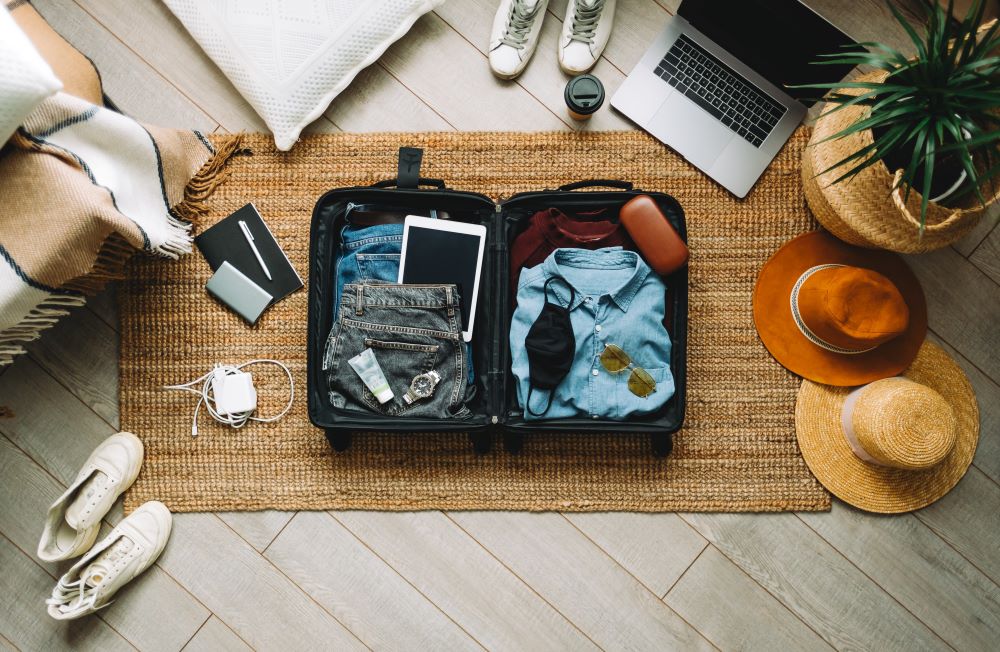 Offener, gepackter Koffer voll mit Klamotten und Elektronik auf einem Teppich. 
