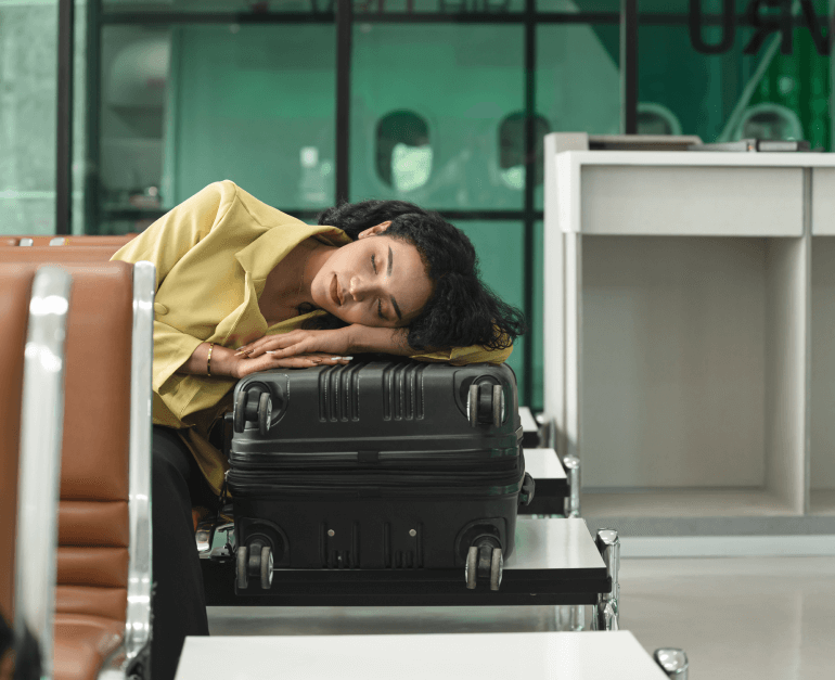 Frau schläft auf Koffer am Flughafen