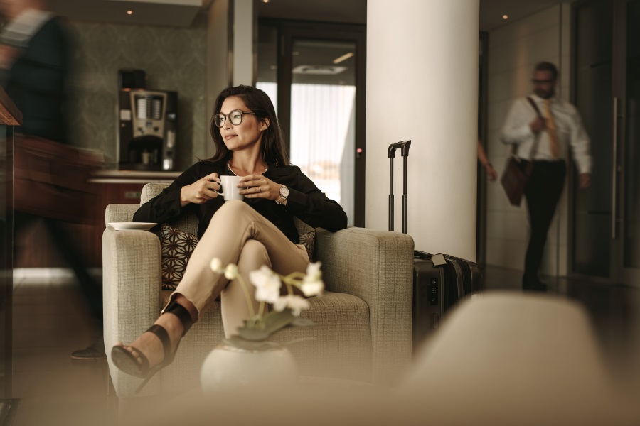 Frau sitzt mit Kaffeetasse in einer Business Hotel Lobby.