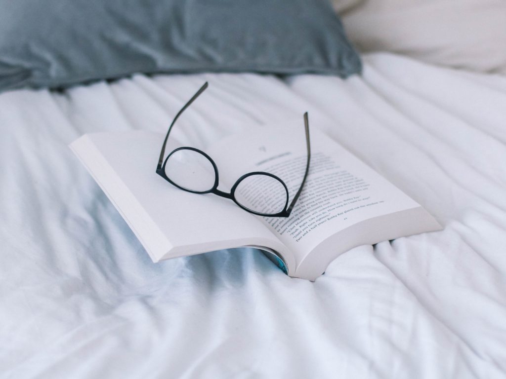 Book with glasses on bed