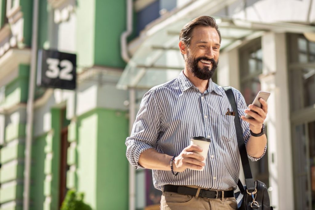 Mitarbeiter mit Smartphone und Kaffee auf dem Weg zur Arbeit